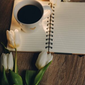 Cup of Coffee, open book and a bouquet tulip flowers over wood table top. Composition with copy space.