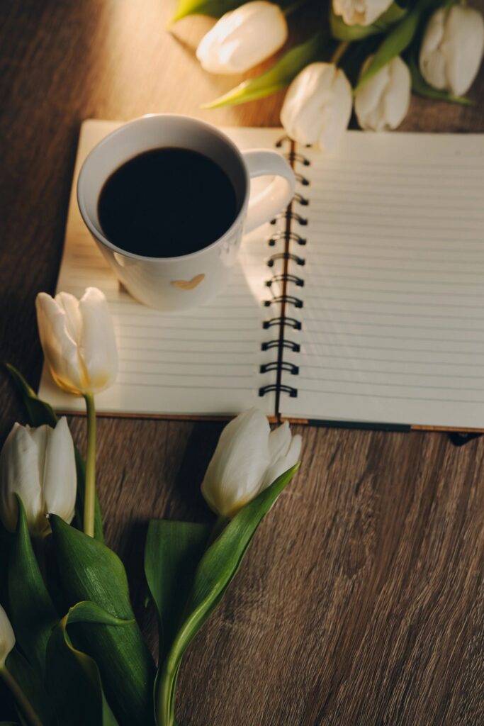 Cup of Coffee, open book and a bouquet tulip flowers over wood table top. Composition with copy space.