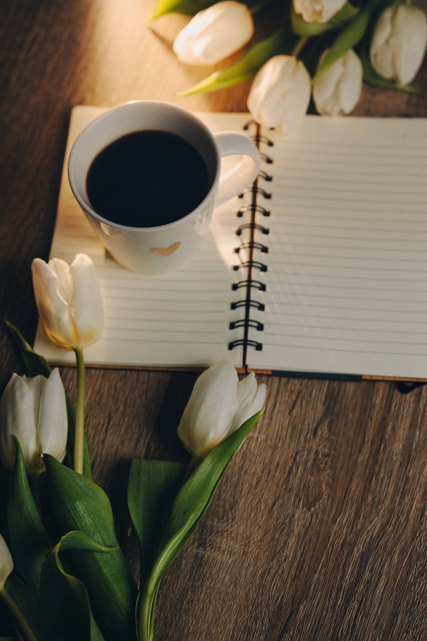 Cup of Coffee, open book and a bouquet tulip flowers over wood table top. Composition with copy space.