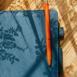 Orange Pen On Notebook With Sunlight Shadows