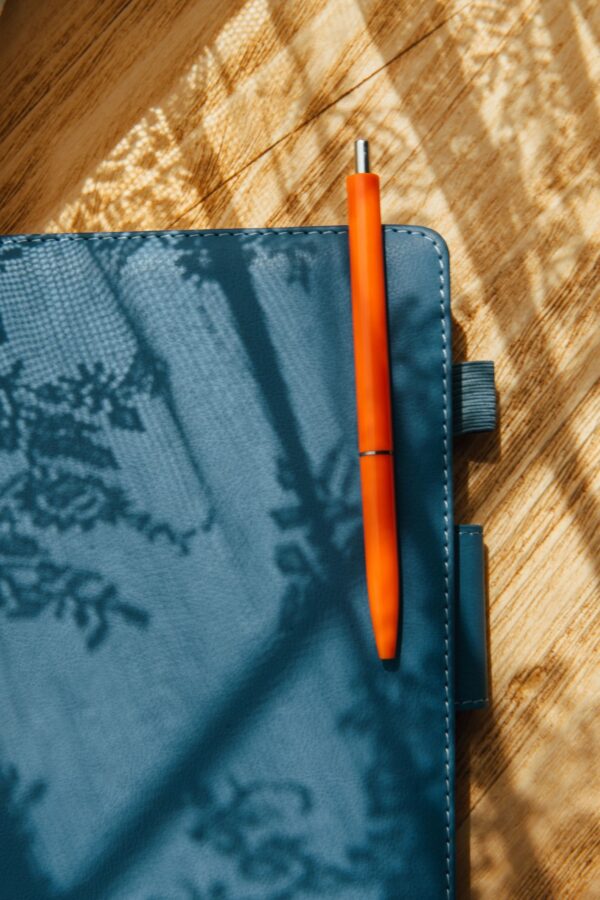 Orange Pen On Notebook With Sunlight Shadows
