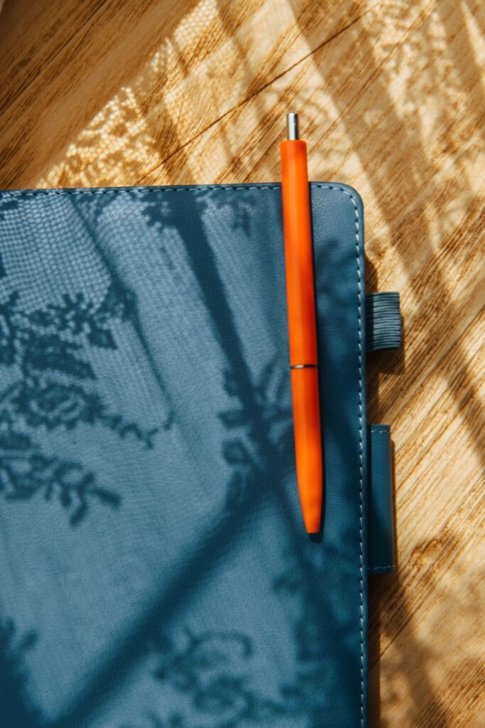 Orange Pen On Notebook With Sunlight Shadows